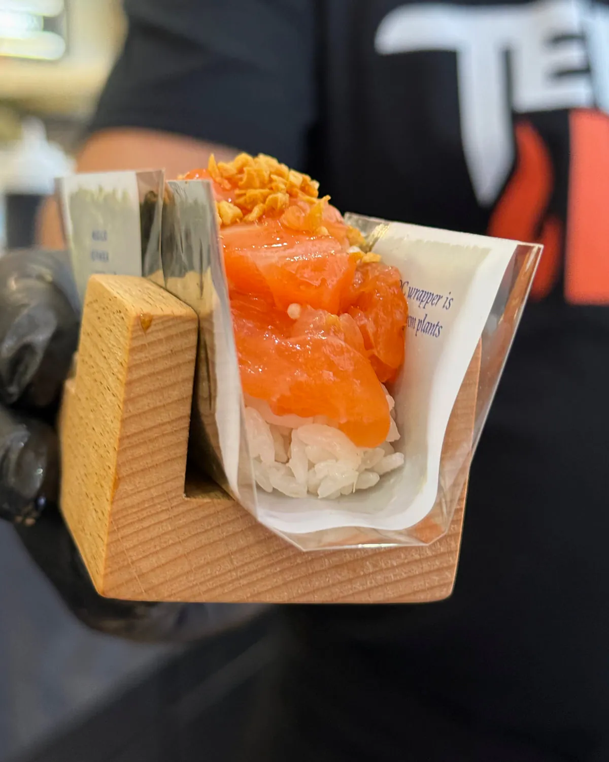 A salmon hand roll held out across the counter in its wrap