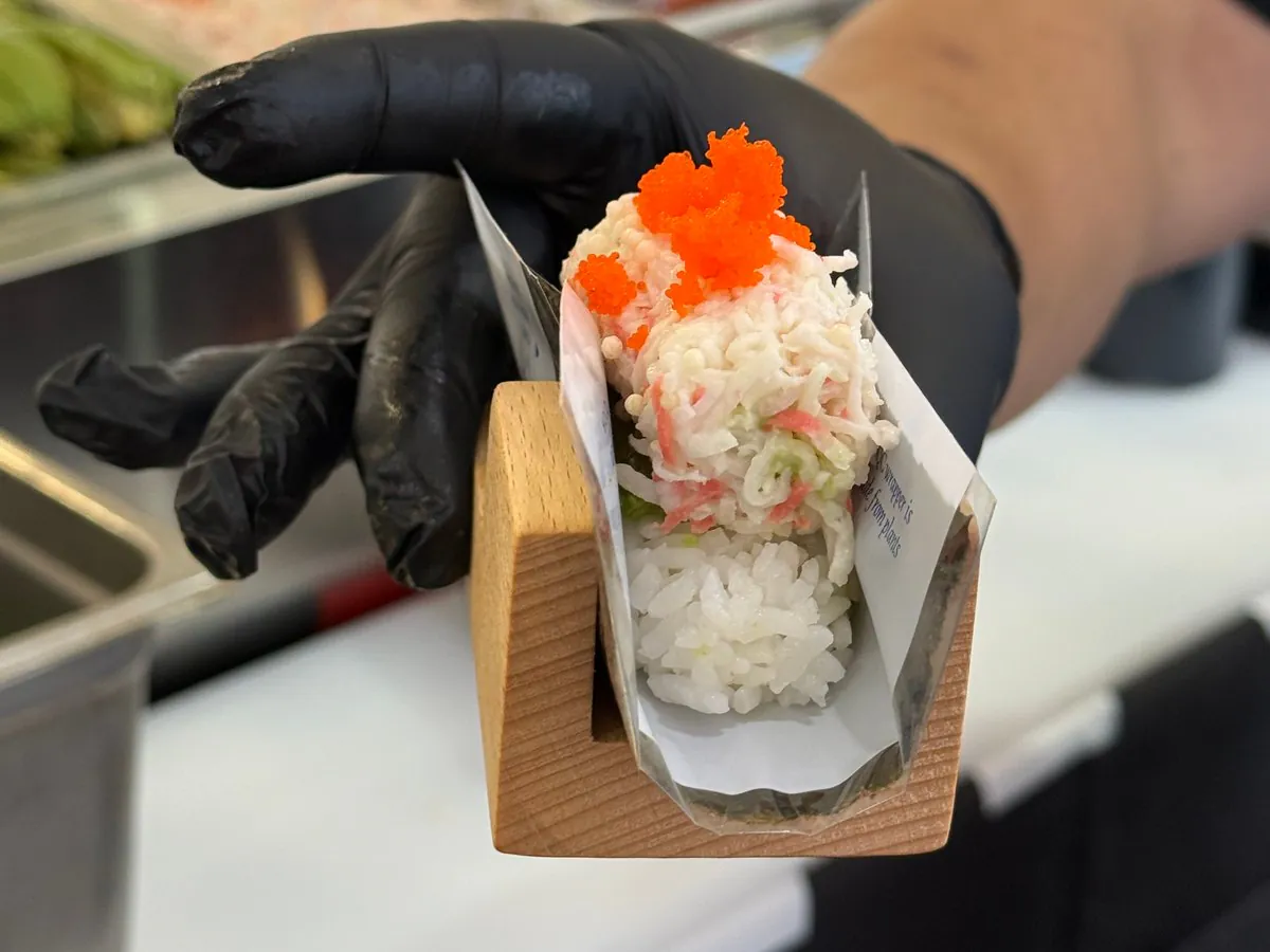 A hand roll in its wooden stand, held out across the counter