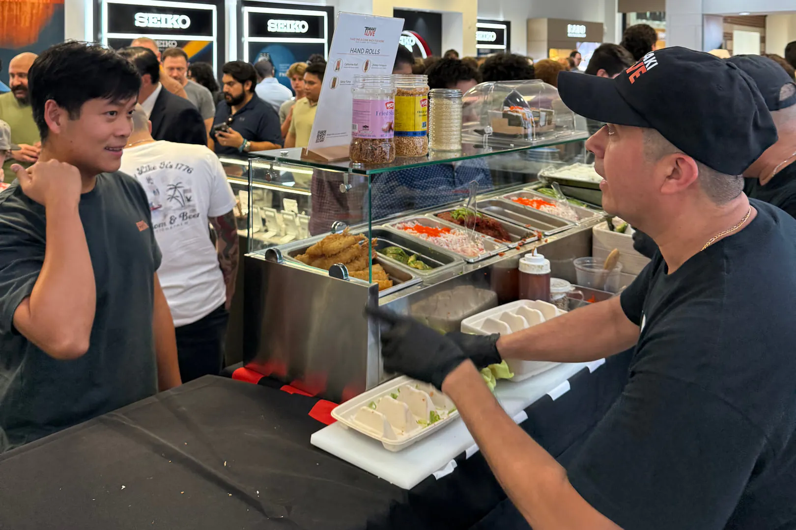 A chef handing a tray of hand rolls across the Temaki Live counter at a corporate event