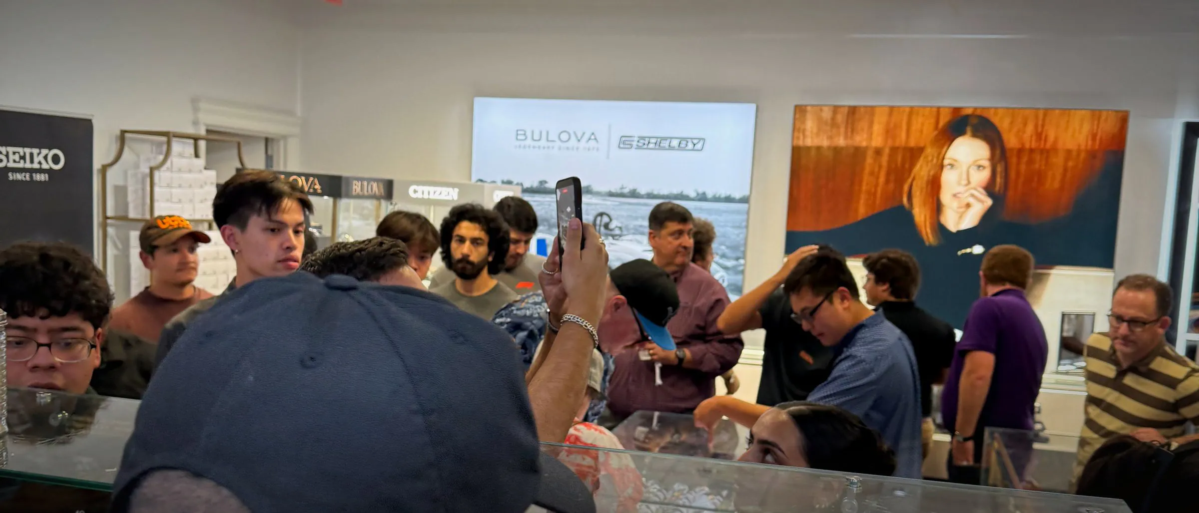 A crowded showroom seen over a chef's shoulder, guests holding up phones to film the counter