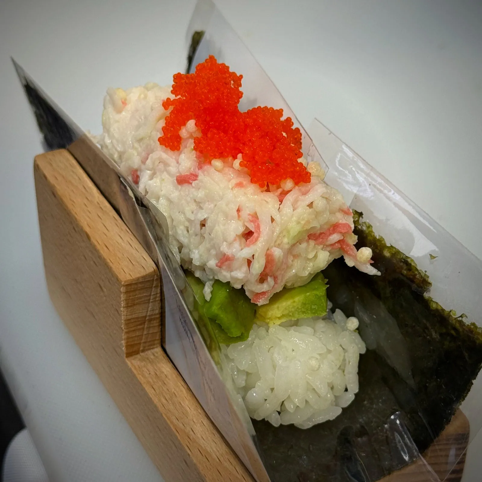 A California hand roll with tobiko standing in its wooden holder