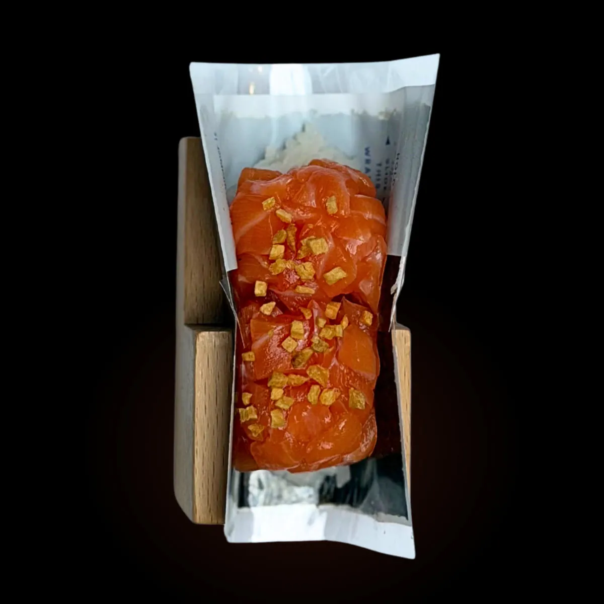 A salmon hand roll in its stand against black