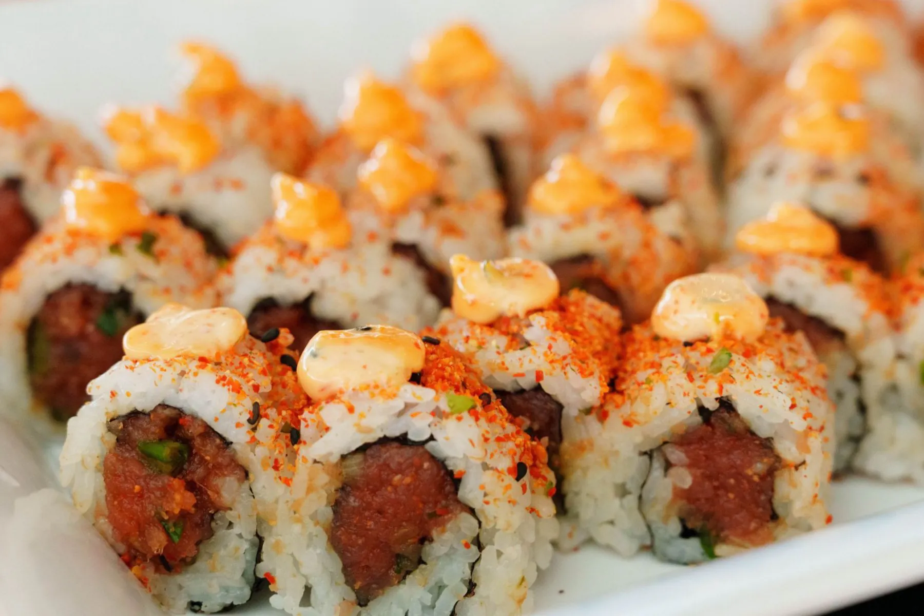 A sharing tray of spicy tuna maki, cut faces up, spicy mayo and togarashi on top