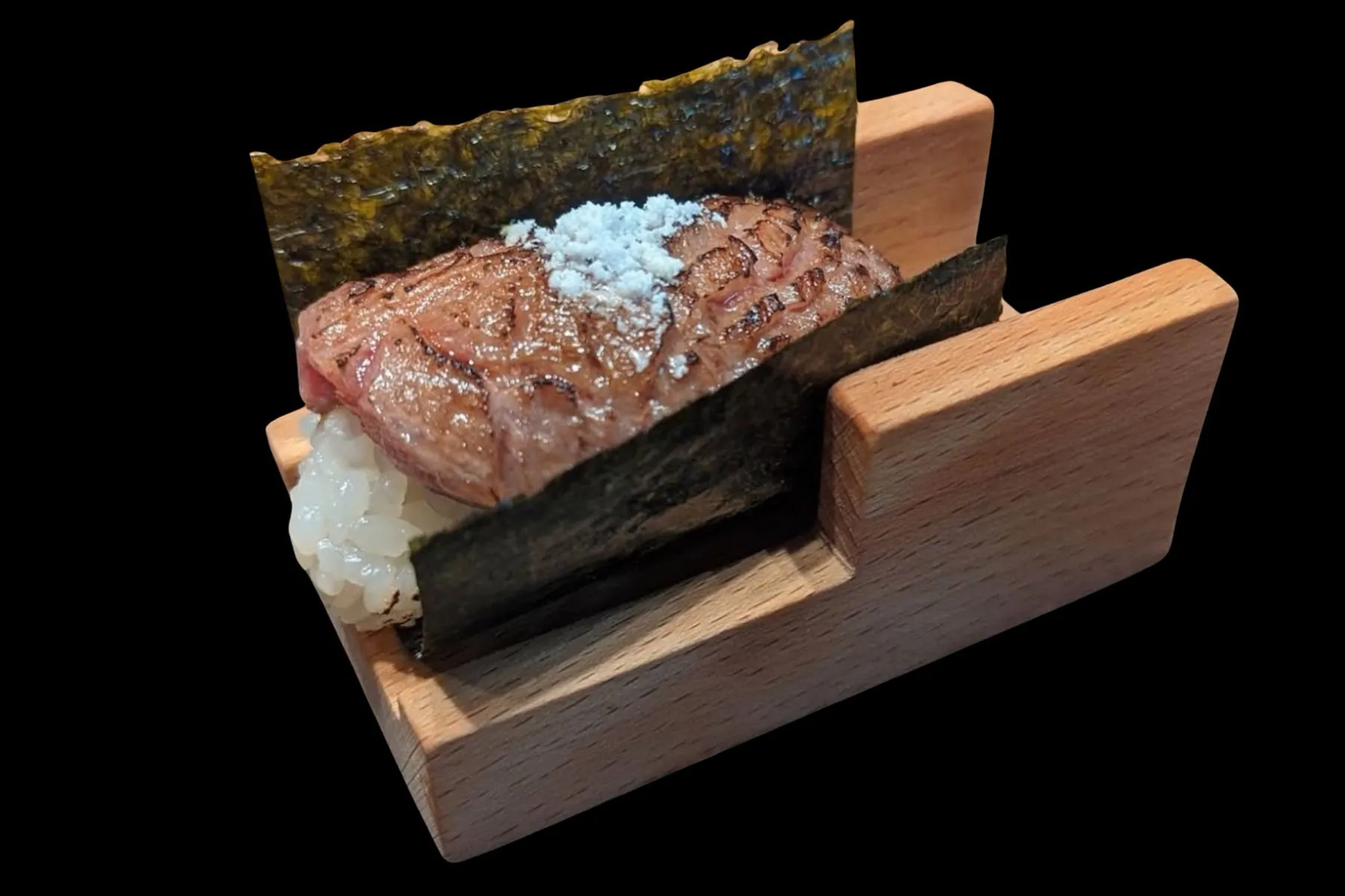Seared wagyu hand roll finished with sea salt, in a wooden stand against black